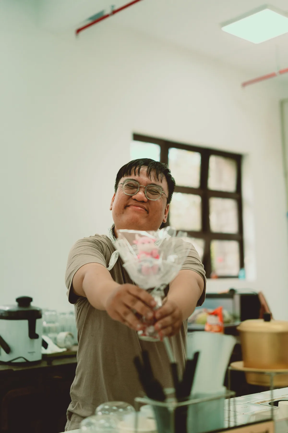 A person in an apron smiling and holding out a wrapped flower.