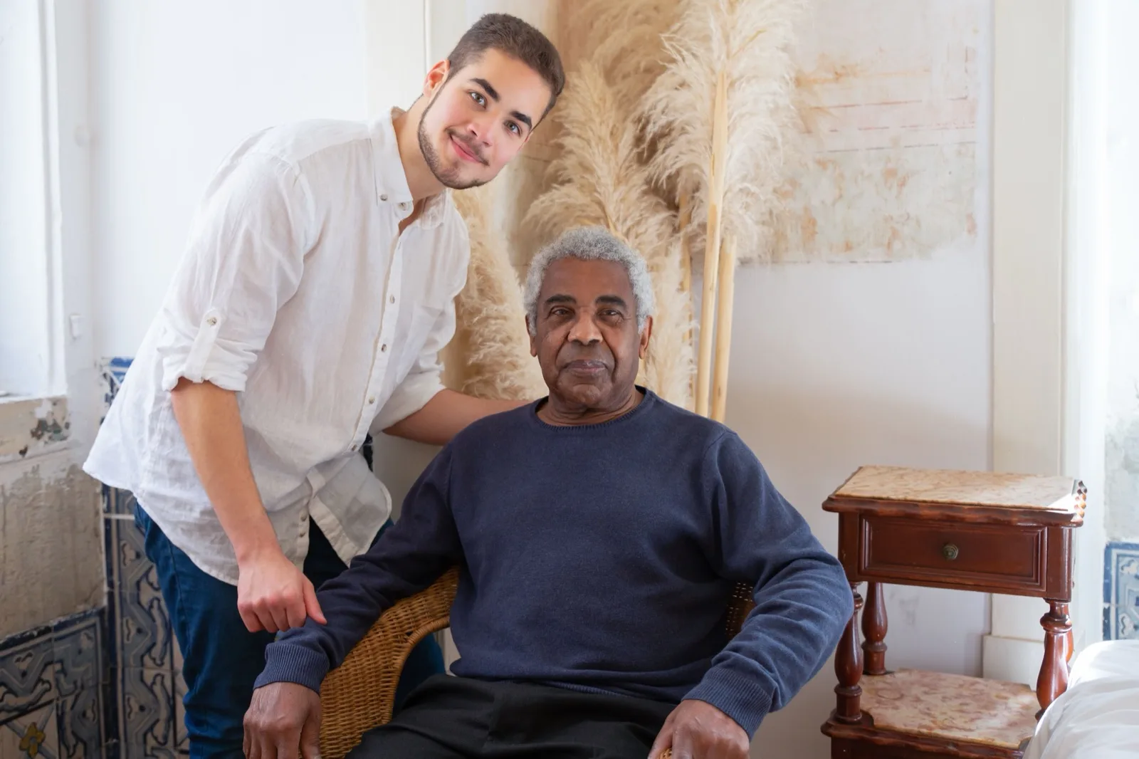 An older man seated in a chair with a younger man standing beside him.